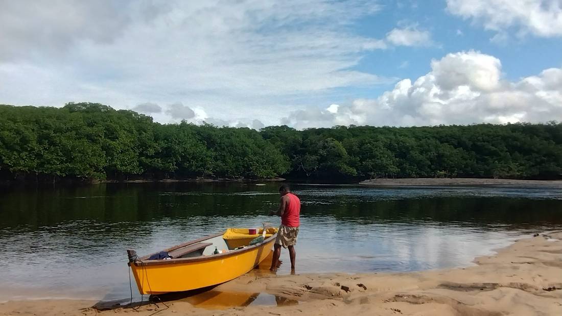 O pescador ao lado do barco amarelo, encostado no banco de areia do rio
